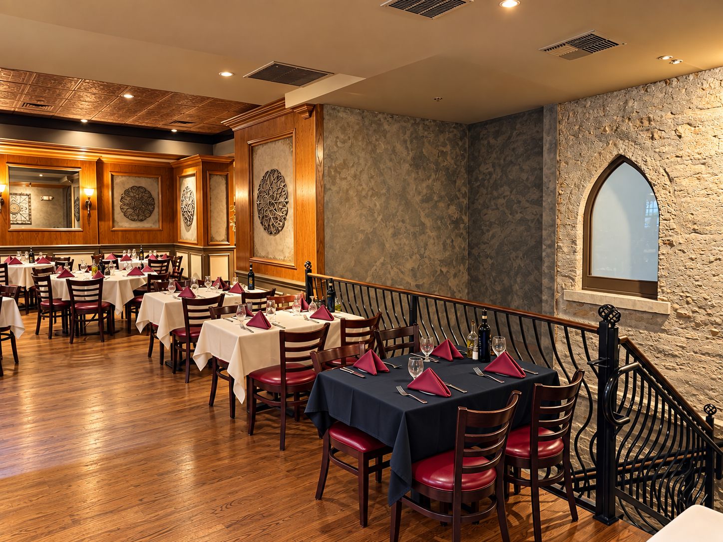 Nuova Italia's main dining room with stone walls, an arched window and tables set with burgundy napkins